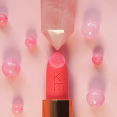 Pink lipstick with gold cap on a pink background with blurred pink beads