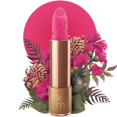 A gold-colored tube of natural lipstick with a pink label, displayed in front of a floral background.